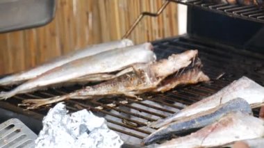 An African American cooks raw fish on the grill. African traditional food at street food festival.