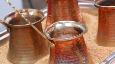 Ready freshly brewed turkish coffee in a turk on the sand, four copper turks close up view.