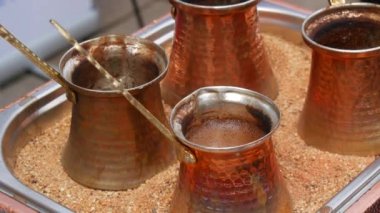 Ready freshly brewed turkish coffee in a turk on the sand, four copper turks close up view.