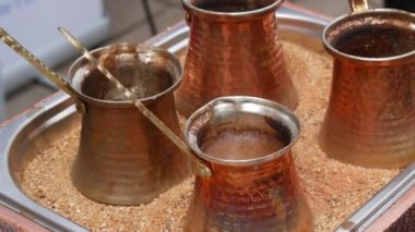 Four copper coffee turks brew Turkish coffee on the sand.