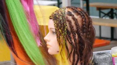 Hairdressing training wig head, lots of African multi-colored braids on the background of artificial hair curls in the street.