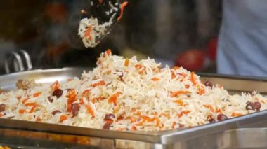 A large dish of rice is being prepared at an open air outdoor food festival. Pilaf is mixed with a special kitchen spatula.