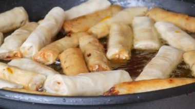 Asian spring rolls are fried in oil in a pan and turned over with kitchen tongs.