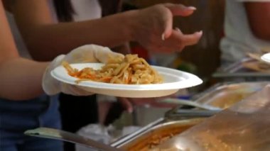 A female chef hand pours thai noodles into a disposable plastic plate at an outdoor food festival.