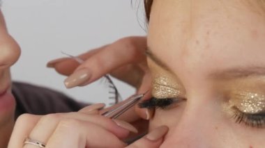 Beautiful bright professional makeup in a beauty studio. Make-up artist glues artificial long eyelashes to give expressiveness to the eyes, close-up view.