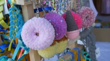 Many bracelets from blue-yellow ribbons in symbols and souvenirs of Ukraine on support stand in tent of Ukraine at the fair nearby handmade crochet keychains in the form of sweets ice cream donuts.