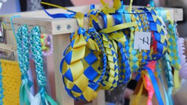 Many bracelets from blue-yellow ribbons in symbols and souvenirs of Ukraine on the support stand in the tent of Ukraine at the fair