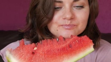 A young beautiful woman with an appetite eats a slice of red ripe juicy watermelon, the juice flows through her mouth, her face is stained in watermelon juice.