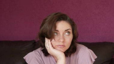 A young beautiful woman is sitting with her face propped up with her hand, bored and looking at the camera. Emotions of a woman longing and boredom.