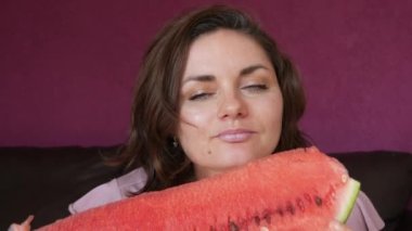 A young beautiful woman with an appetite eats a slice of red ripe juicy watermelon, the juice flows through her mouth, her face is stained in watermelon juice.