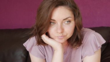 A young beautiful woman is sitting with her face propped up with her hand, bored and looking at the camera. Emotions of a woman longing and boredom.