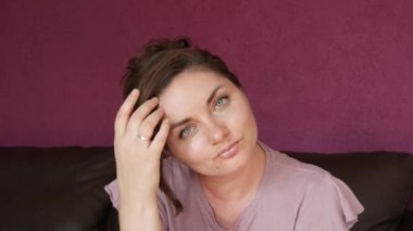 Close-up portrait of a young beautiful woman with green eyes and dark hair, who looks directly into the camera Seriously and slyly looking at the camera on a leather sofa in the room.