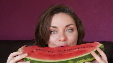 A young beautiful woman with an appetite eats a slice of red ripe juicy watermelon, the juice flows through her mouth, her face is stained in watermelon juice.