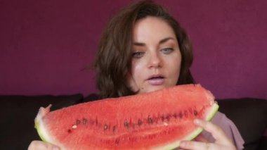 A young beautiful woman with an appetite eats a slice of red ripe juicy watermelon, the juice flows through her mouth, her face is stained in watermelon juice.