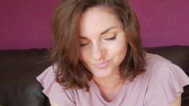 Close-up portrait of a young beautiful woman with green eyes and dark hair, who looks directly into the camera Seriously and slyly looking at the camera on a leather sofa in the room.