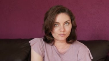 A young beautiful woman is sitting with her face propped up with her hand, bored and looking at the camera. Emotions of a woman longing and boredom.