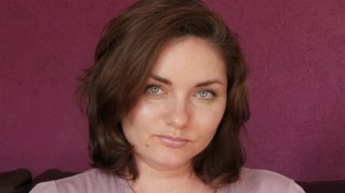 Close-up portrait of a young beautiful woman with green eyes and dark hair, who looks directly into the camera Seriously and slyly looking at the camera on a leather sofa in the room.