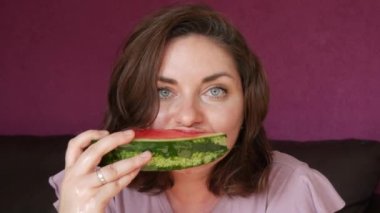 A young beautiful woman with an appetite eats a slice of red ripe juicy watermelon, the juice flows through her mouth, her face is stained in watermelon juice.