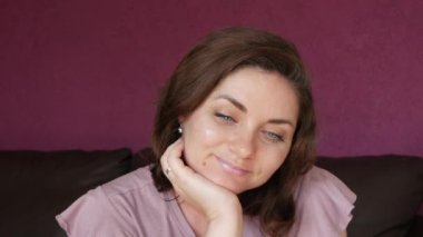 Close-up portrait of a young beautiful woman with green eyes and dark hair, who looks directly into the camera with tenderness and smiles, touches her face and hair