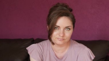 Close-up portrait of a young beautiful woman with green eyes and dark hair, who looks directly into the camera Seriously and slyly looking at the camera on a leather sofa in the room.