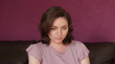 Close-up portrait of a young beautiful woman with green eyes and dark hair, who looks directly into the camera Seriously and slyly looking at the camera on a leather sofa in the room.