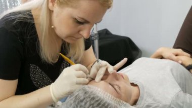A master with blond hair makes eyebrow correction to his client, and applies a special pigment that is on her finger in the ring. Microblading, permanent makeup, tattoo, new form of eyebrows, beauty