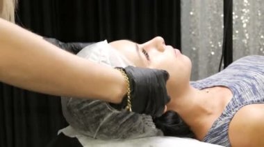 The beginning of the procedure. The girl is put on a special cosmetic cap. Eyebrow shape correction. Microblading, permanent makeup, tattoo