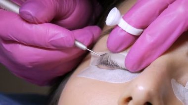 Profesyonel bir güzellik salonunda modern kirpik temizleme prosedüründen önce genç bir kızın yüzü. Pembe lastik eldivenlerle kirpik kıvırma prosedüründen önce usta özel yapıştırıcı uyguluyor..