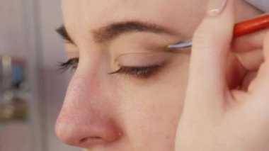 Parlak dumanlı göz makyajlı genç bir kadın modelin güzel anlamlı gözleri. Kendini adamış makyaj fırçası göz alıcı koyu bir bukalemun göz farı sürmektedir..