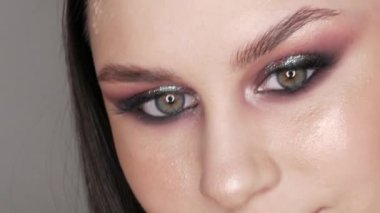 Şık makyajlı, dumanlı, poz veren ve gülümseyen güzel genç kız modeli, gri arka planda yüksek moda..