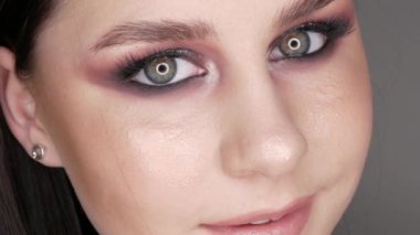 Şık makyajlı, dumanlı, poz veren ve gülümseyen güzel genç kız modeli, gri arka planda yüksek moda..