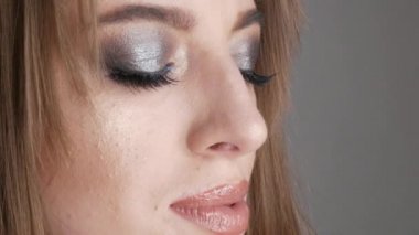 Güzel, parlak akşam makyajlı, mavi gölgeli, mavi taşlı ve stüdyodaki kameraya poz veren genç bir manken. Kameraya bak.