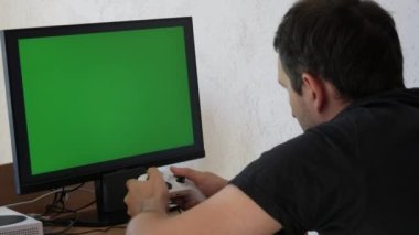 Young male gamer playing game console using joystick remote control over green screen monitor tv chroma key at home. Man Focused Gaming in Living Room