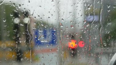 Rain on glass of a bus or car. Raindrops run down the window. Background of a city street, road. Drive car on traffic jam street at rain storm, inside a car driving,blurred traffic light background