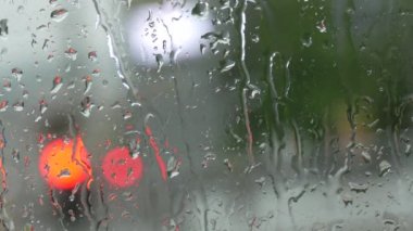 Rain on glass of a bus or car. Raindrops run down the window. Background of a city street, road. Drive car on traffic jam street at rain storm, inside a car driving,blurred traffic light background