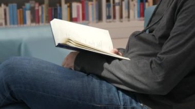 Hands of a man holding a book in a bookstore or library on a background with many different bookshelves.