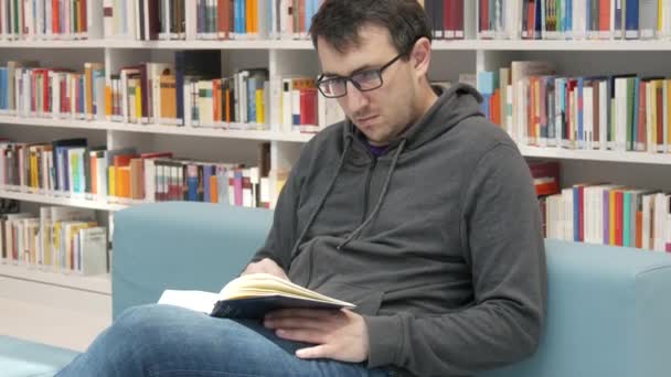 Young Handsome Intelligent Man Glasses Reads Book Bookstore Library Background — Stock video