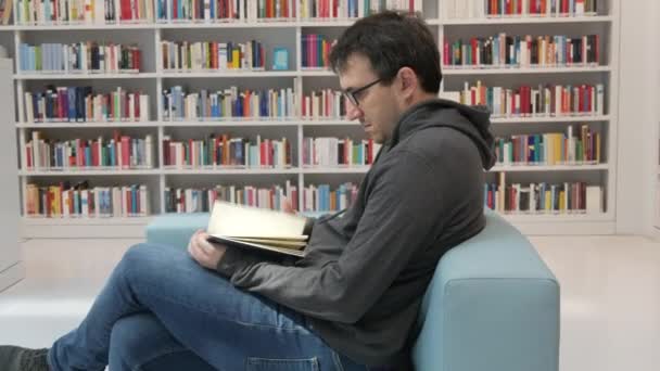 Young Handsome Intelligent Man Glasses Reads Book Bookstore Library Background — Αρχείο Βίντεο