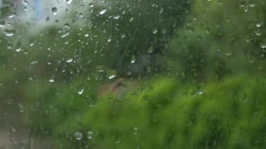 Rain on glass of a bus or car. Raindrops run down the window. Background of a city street, road. Drive car on traffic jam street at rain storm, inside a car driving,blurred traffic light background