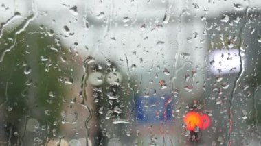 Rain on glass of a bus or car. Raindrops run down the window. Background of a city street, road. Drive car on traffic jam street at rain storm, inside a car driving,blurred traffic light background