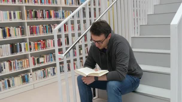 Young Handsome Intelligent Man Glasses Reads Book Bookstore Library Background — Stock video