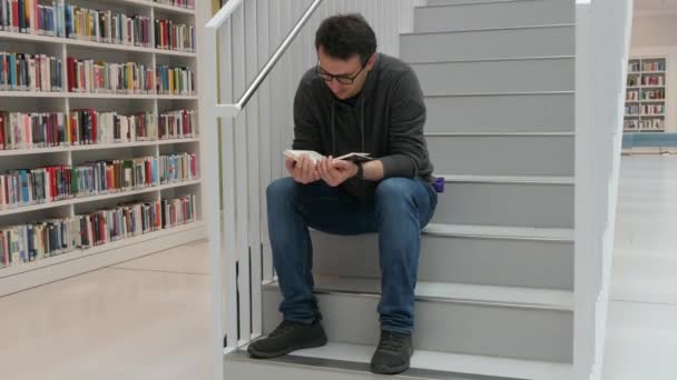 Young Handsome Intelligent Man Glasses Reads Book Bookstore Library Background — Stock video