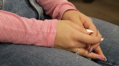 The well-groomed hands of a young girl lie on their knees, with multi-colored painted nails