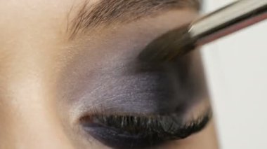 Close up view of makeup artist makes models smoky eyes with the help of special brush blue eyeshadow, eyes and eyelashes of a girl. Professional high fashion.