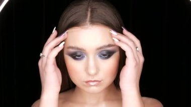 Portrait of a very beautiful long-haired delightful young girl model with bright evening make-up, smoky eyes posing in front of the camera on a stylish black background
