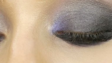 Close up view of makeup artist makes models smoky eyes with the help of special brush blue eyeshadow, eyes and eyelashes of a girl. Professional high fashion.