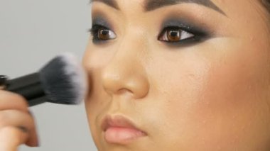 Profesyonel makyaj sanatçısı özel bir fırça ile Asya Koreli modeller yüz vakıf kapatıcı veya vurgulayıcı uygular