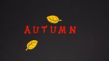 Stop motion animation. Falling yellow leaves on a black background and lettering autumn. Autumn concept, change of season.