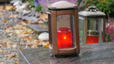 Red memorial candle burning with fire on rainy day on tombstone in cemetery autumn, rainy day. Grave with tombstone on which raindrops falling, against abackground of yellow foliage. Day of all dead.