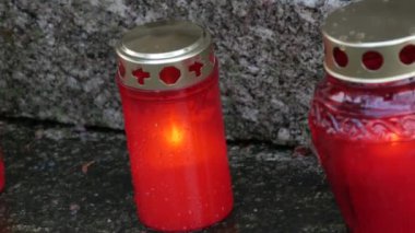 Yağmurlu bir günde yanan kırmızı mum mezarlıkta mezar taşında sonbaharda, yağmurlu günde. Üzerine yağmur damlalarının yağdığı mezar taşıyla birlikte. Tüm ölülerin günü.